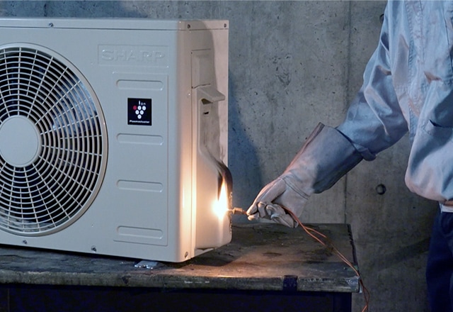 室外機に火が燃え移っても、燃え広がらないことを確認しているイメージ