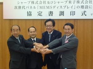 調印式で握手する4者（右から、平井知事、方志専務、鮎川社長、野坂市長）